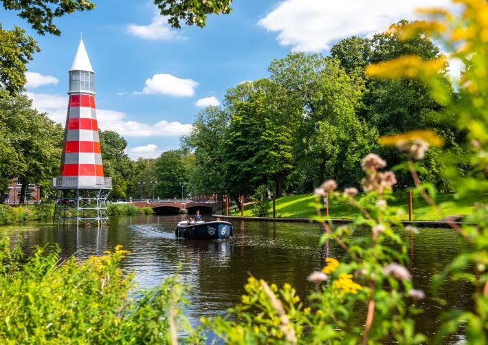 Rode en witte watertoren langs het water in Breda, omringd door groen en bomen met een bootje op de singel